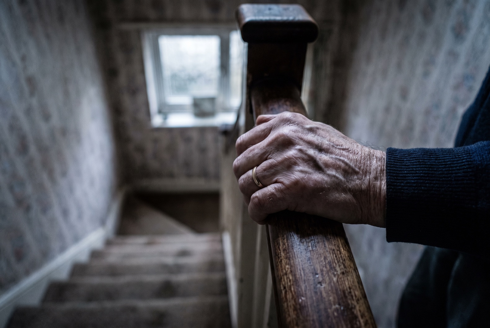 Woman gripping hallway wall with one hand, eyes closed, dizzy